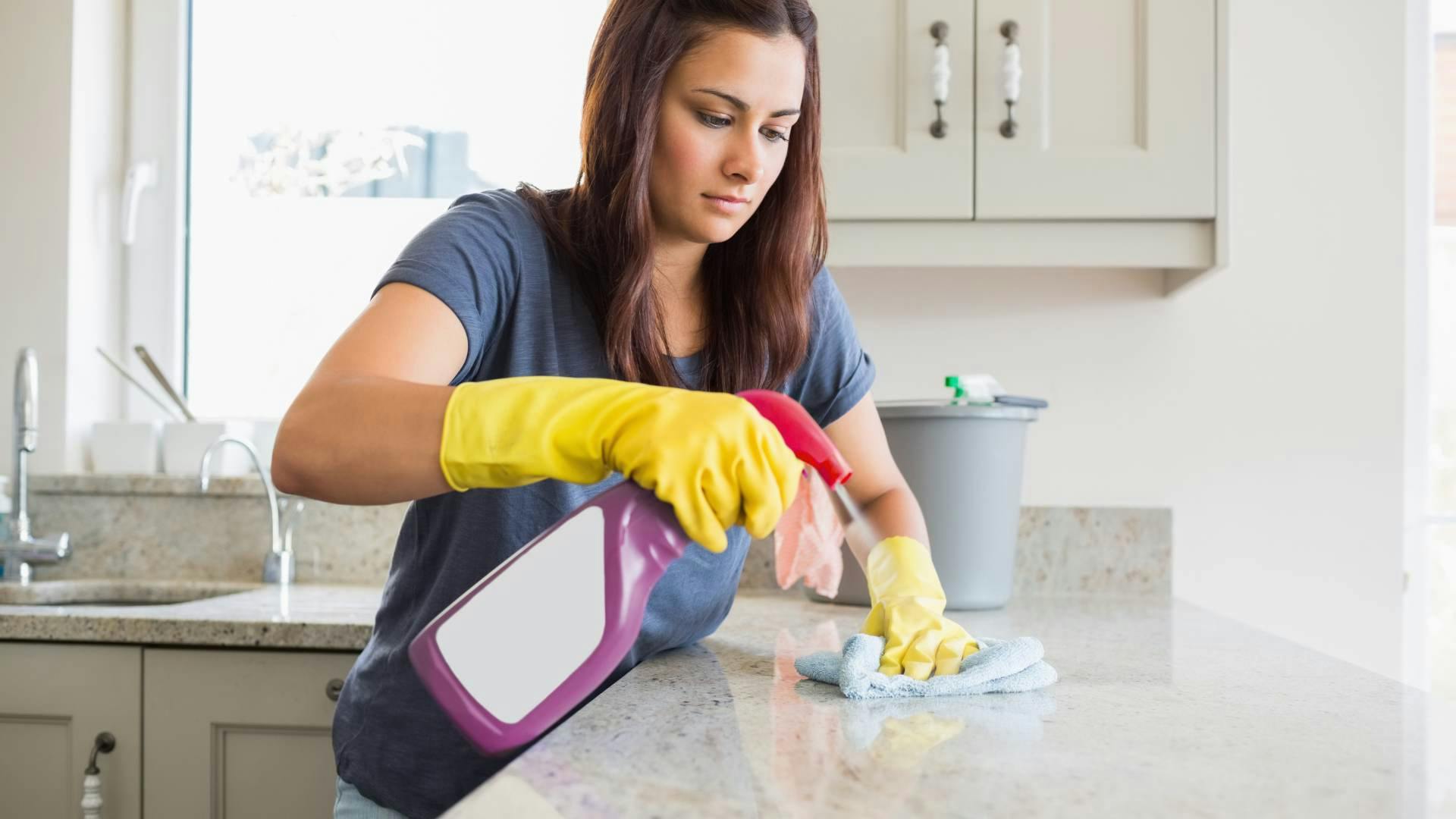 Residential cleaner spraying a sanitizing agent onto a countertop in the kitchen