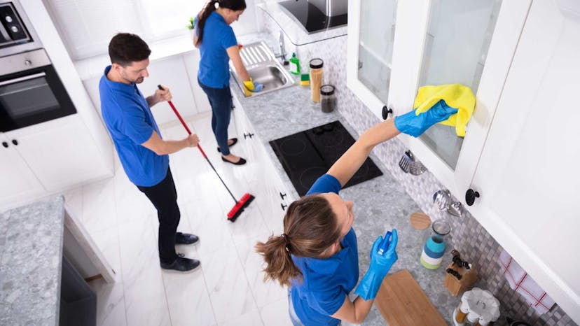 Three residential cleaners in a kitchen sanitizing the sink and drawers and sweeping